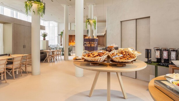 A modern dining area with round tables, wicker baskets of pastries, and a coffee station. - Novotel Brugge Centrum (Bruges)