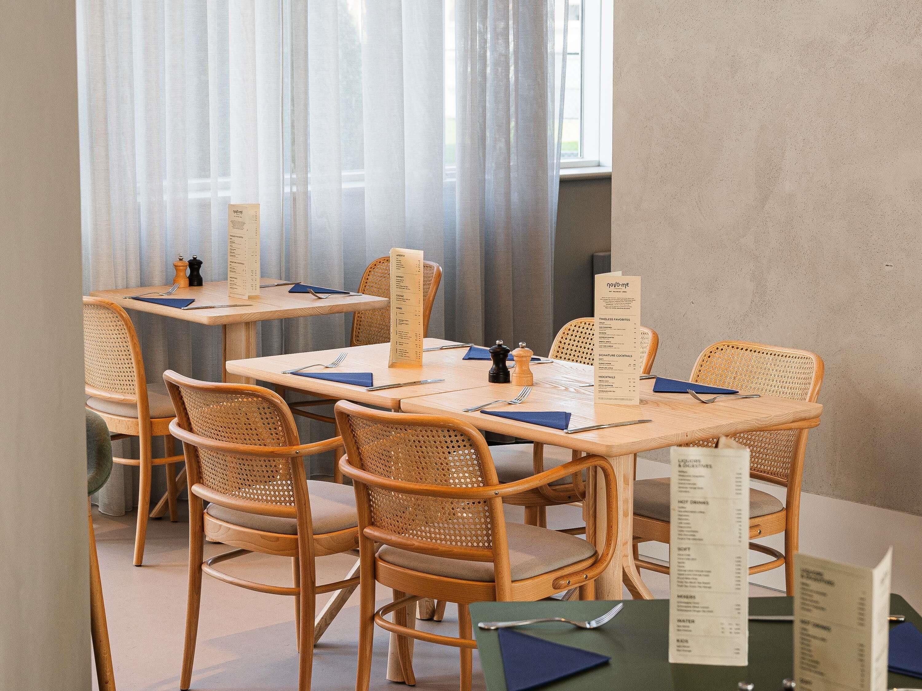 Un espace repas avec des tables et des chaises en bois, des menus et une fenêtre ornée de rideaux légers.