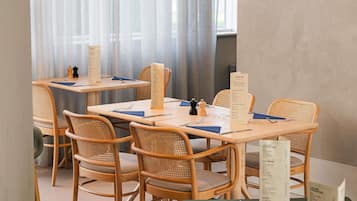 Un espace repas avec des tables et des chaises en bois, des menus et une fenêtre ornée de rideaux légers.