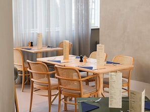 Un comedor con mesas y sillas de madera, menús y una ventana con cortinas translúcidas.
