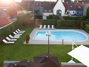 A swimming pool with lounge chairs, a small garden, and a view of residential buildings. - Novotel Brugge Centrum (Bruges)