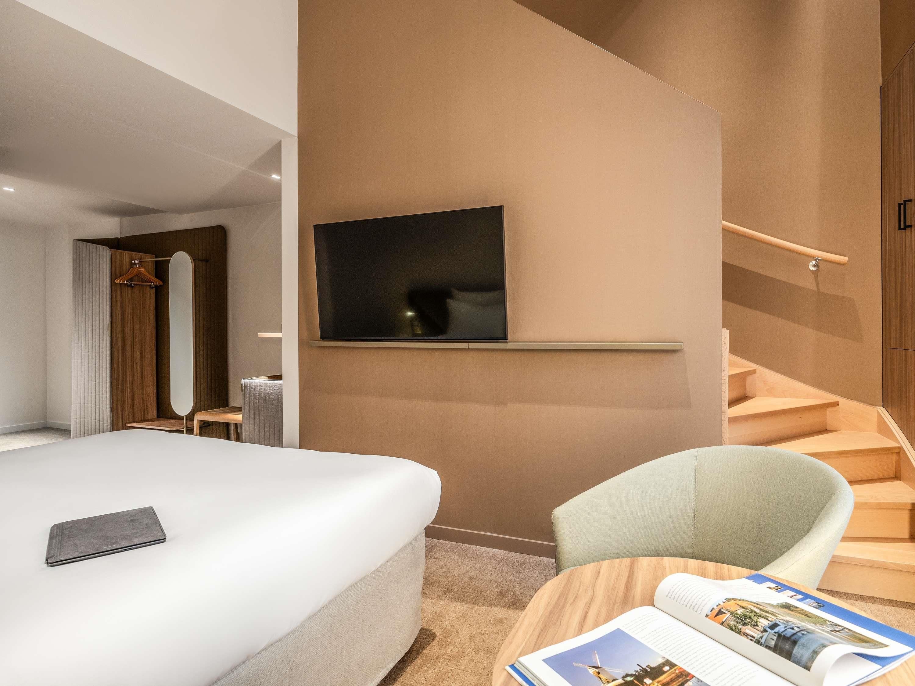Ein modernes Hotelzimmer mit einem großen Bett, einem Flachbildfernseher an der Wand, einem Holzstuhl und einer Treppe.
