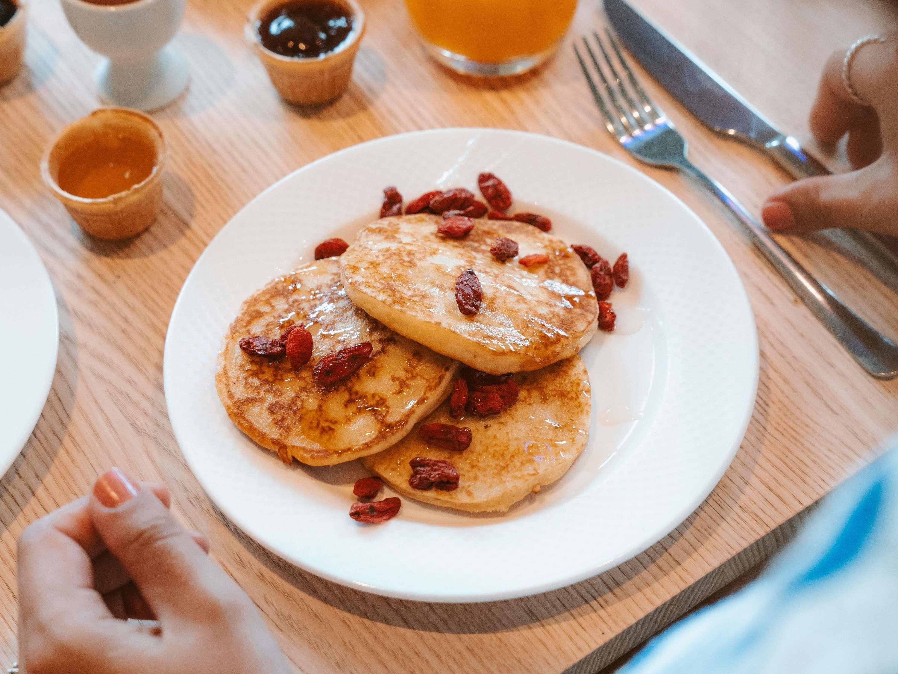 A plate of pancakes with syrup and dried berries.