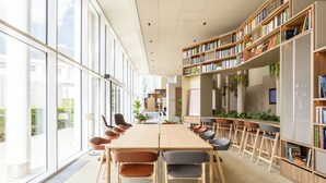 A modern library with a long wooden table, multiple chairs, and bookshelves filled with books. - Novotel Brugge Centrum (Bruges)