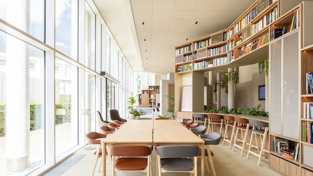 A modern library with a long wooden table, multiple chairs, and bookshelves filled with books. - Novotel Brugge Centrum (Bruges)