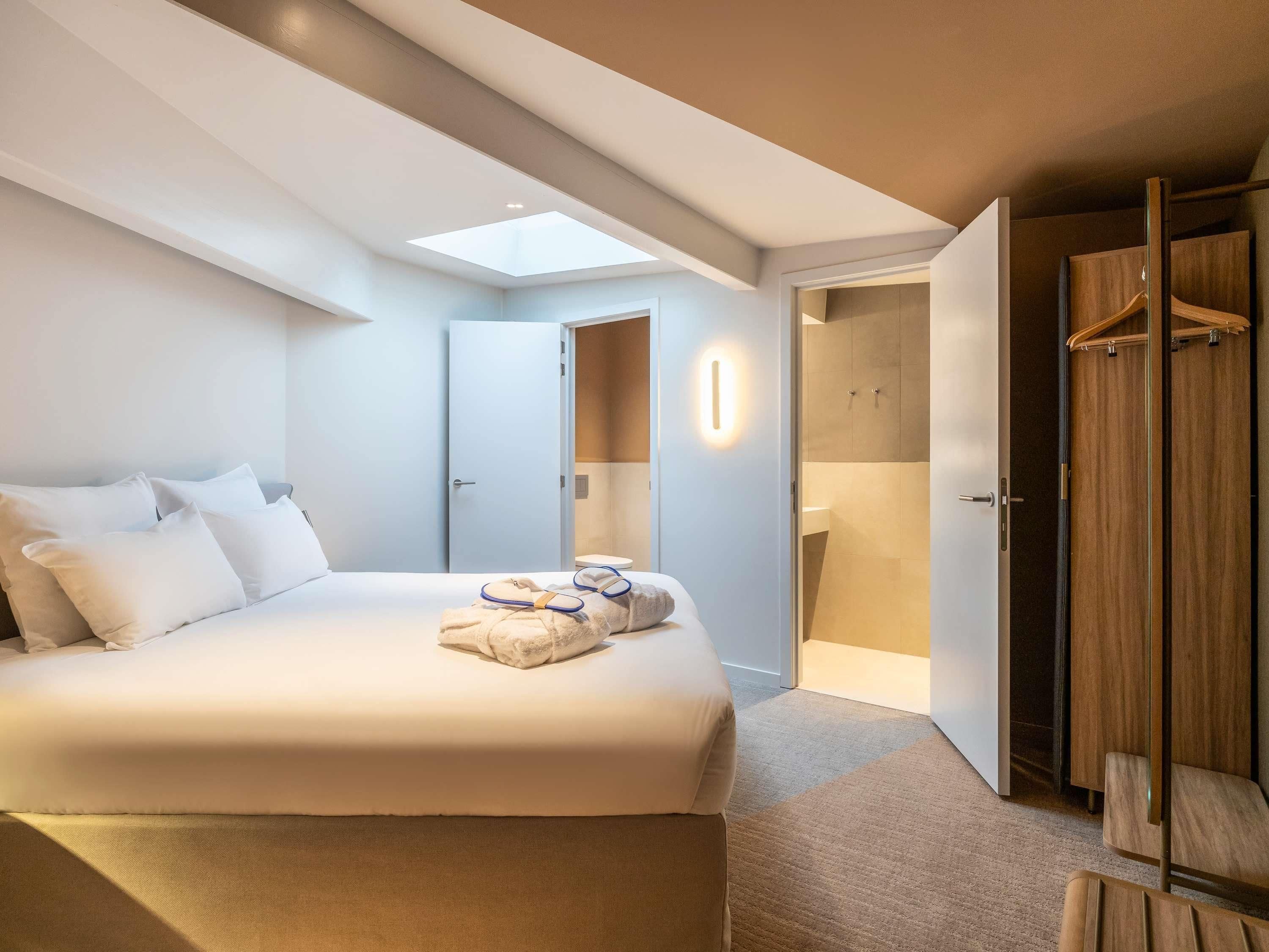 A modern hotel room with a large bed, a skylight, a walk-in closet, and a bathroom.