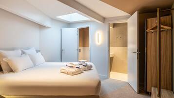 A modern hotel room with a large bed, a skylight, a walk-in closet, and a bathroom.