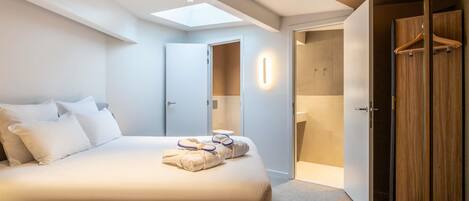 A modern hotel room with a large bed, a skylight, a walk-in closet, and a bathroom.