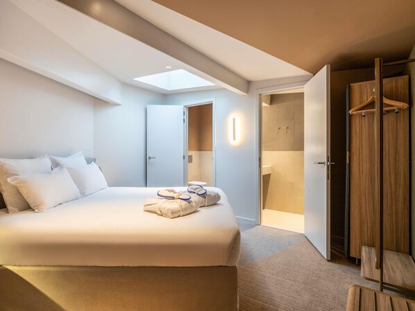 Una habitación de hotel moderna con una cama grande, tragaluces, vestidor y baño.