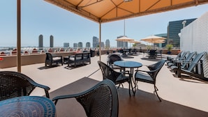 Una terraza en la azotea con mobiliario exterior, sombrillas y vistas del horizonte urbano.