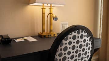 A hotel room with a desk, a lamp, and a chair with a patterned backrest.