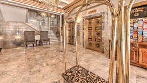 Un vestíbulo imponente con suelos de mármol, candelabros decorados y una zona de estar con tapicería estampada.
