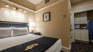 Habitación de hotel con una cama grande, una lámpara de noche, un cuadro en la pared y una pequeña cocina.