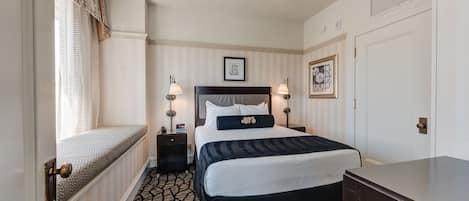 A hotel room with a bed, bedside lamps, a nightstand, a dresser, a window with curtains, and a door.