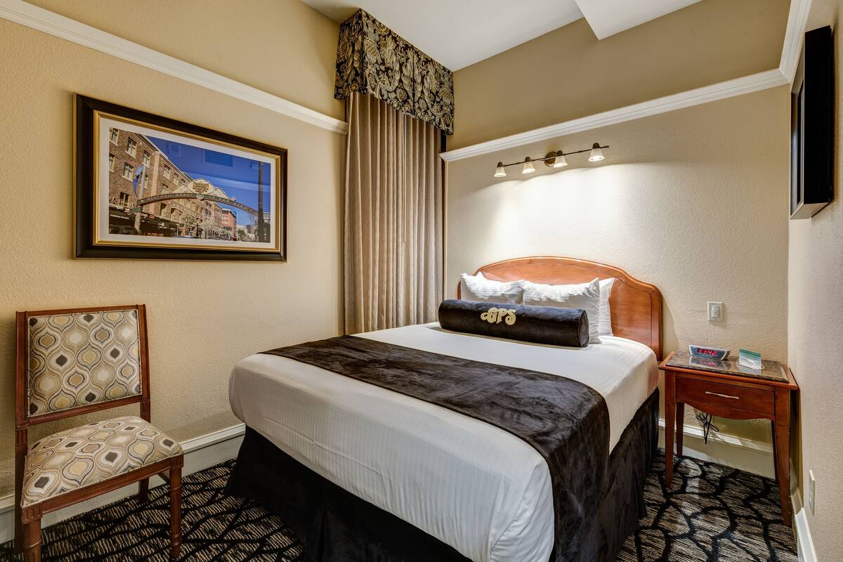 Ein Hotelzimmer mit einem großen Bett, einem Sessel, einem Nachttisch, einem gerahmten Bild an der Wand und einem Fenster mit Vorhängen.