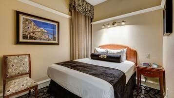 A hotel room with a large bed, a chair, a nightstand, a framed picture on the wall, and a window with curtains.
