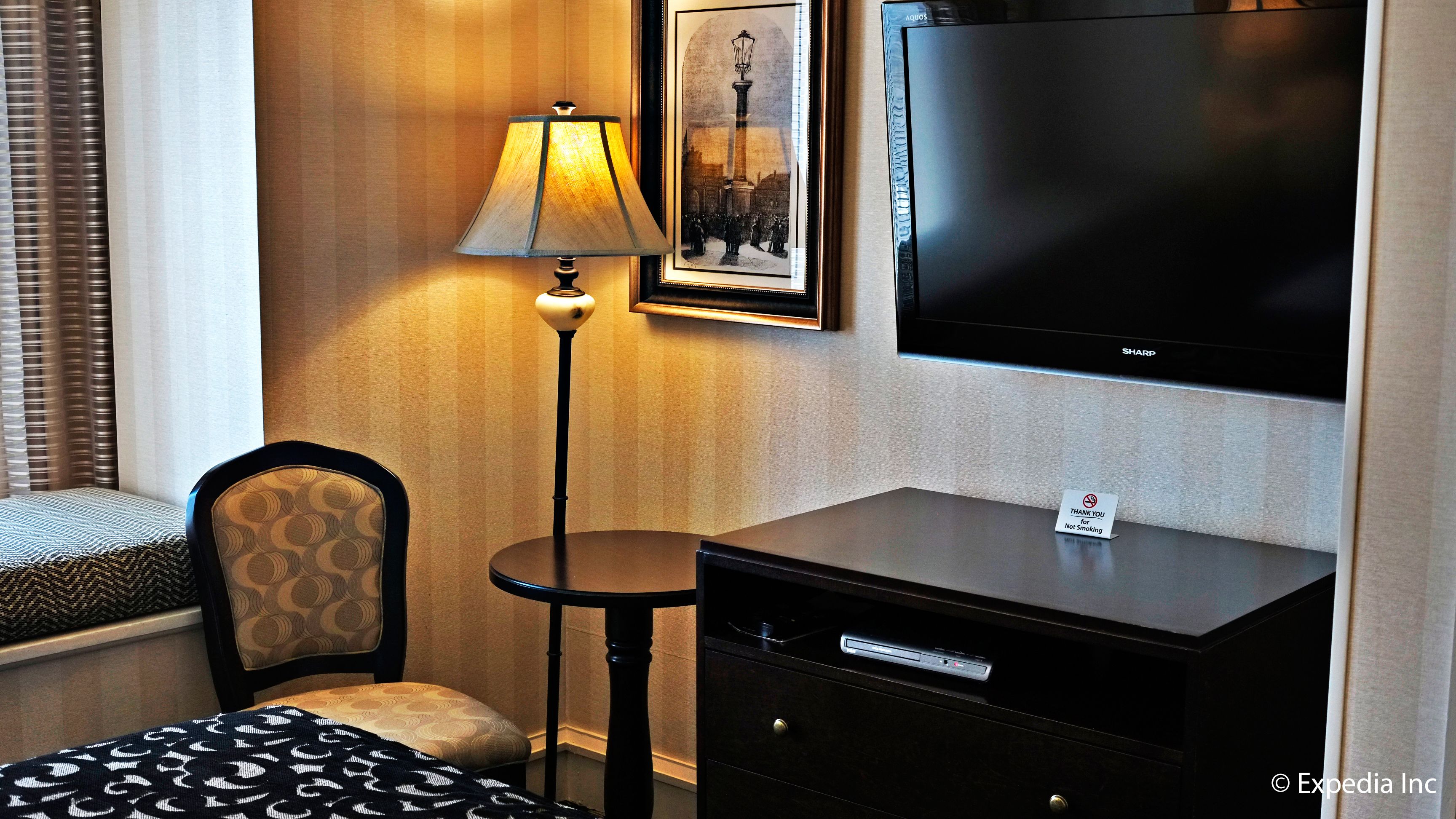 Une chambre d’hôtel avec un lit, un bureau doté d’une lampe, une télévision et un tableau encadré au mur.