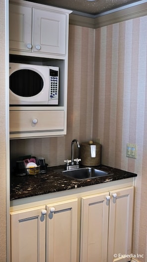 A compact kitchen with a microwave, sink, and cabinets. - Gaslamp Plaza Suites (San Diego)