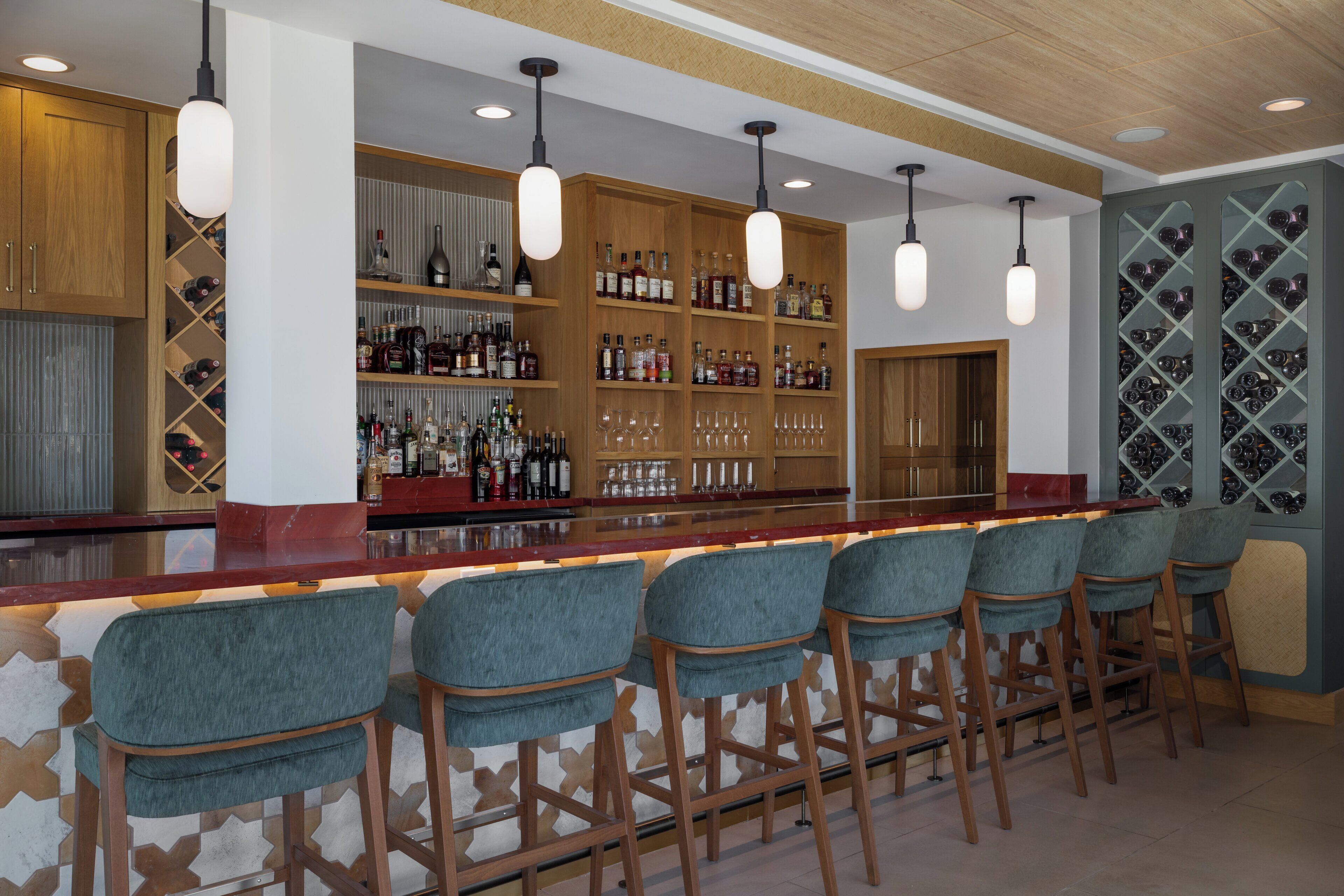 Un espace bar doté d’étagères en bois remplies de bouteilles, d’un comptoir et de plusieurs tabourets de bar.