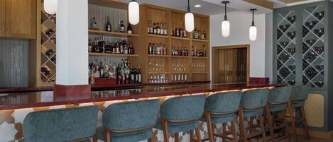 Un espace bar doté d’étagères en bois remplies de bouteilles, d’un comptoir et de plusieurs tabourets de bar.