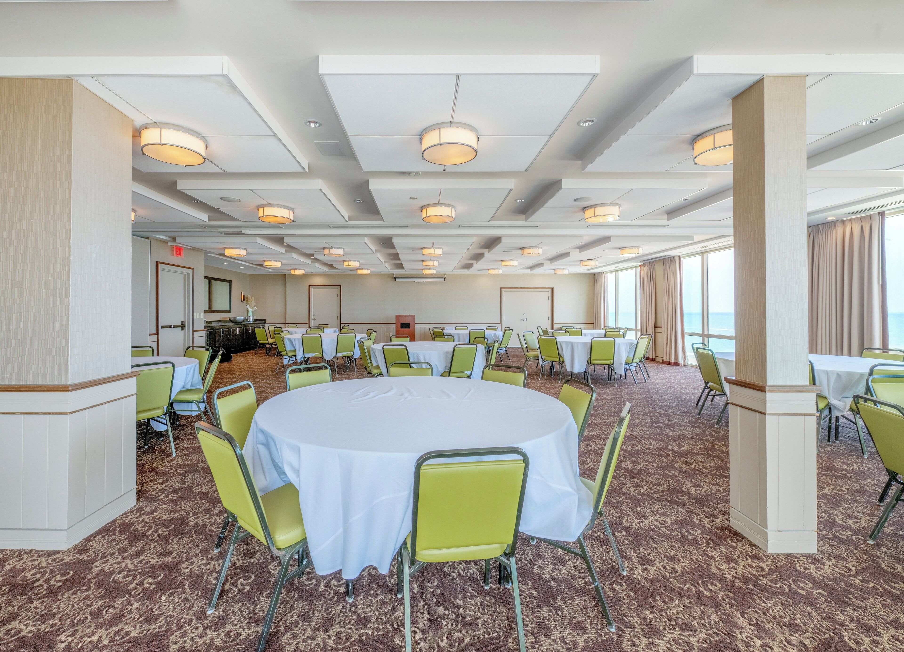 A large conference room with round tables and green chairs, carpeted floor, and ceiling lights.