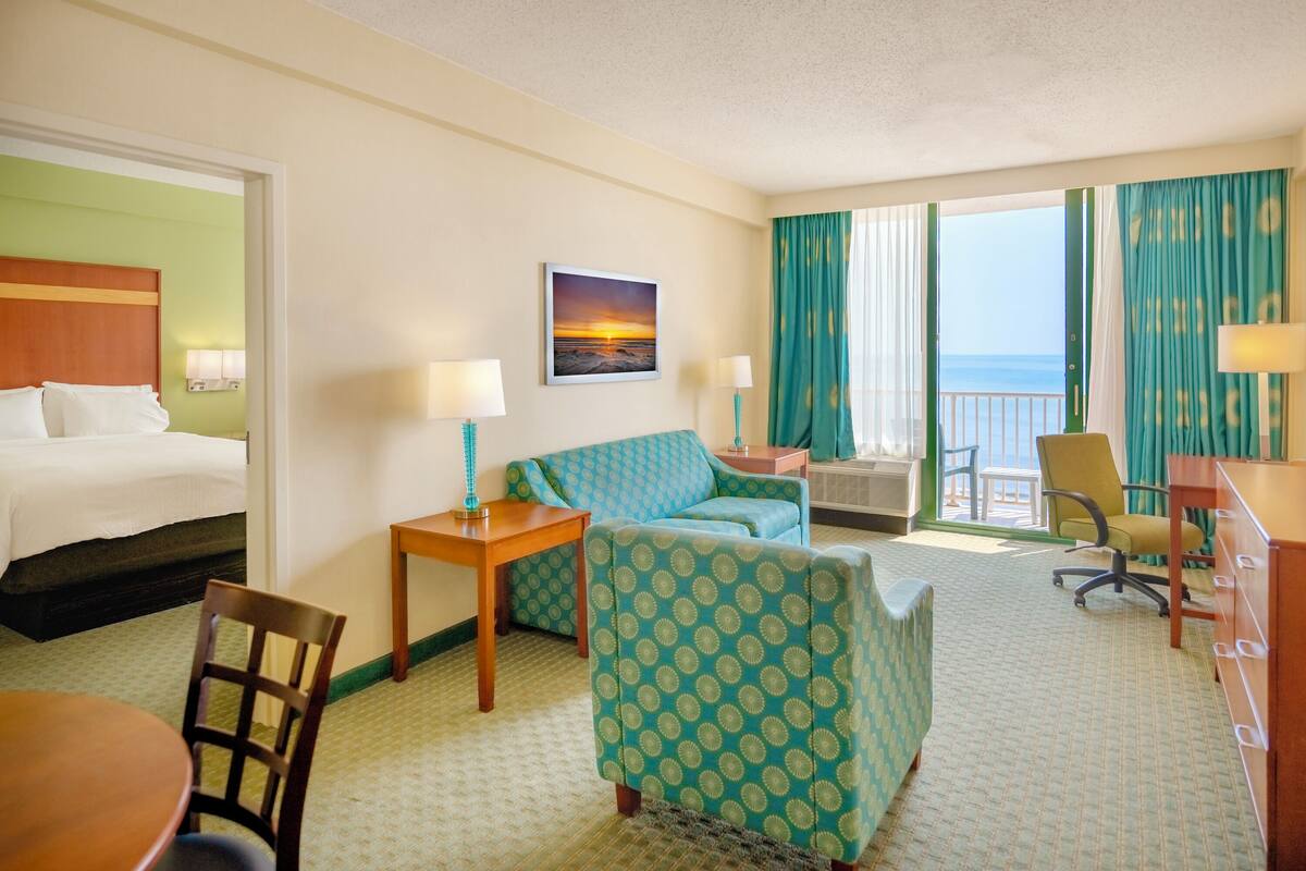 A hotel room with a bed, a sofa, a desk, a chair, and a view of the ocean.