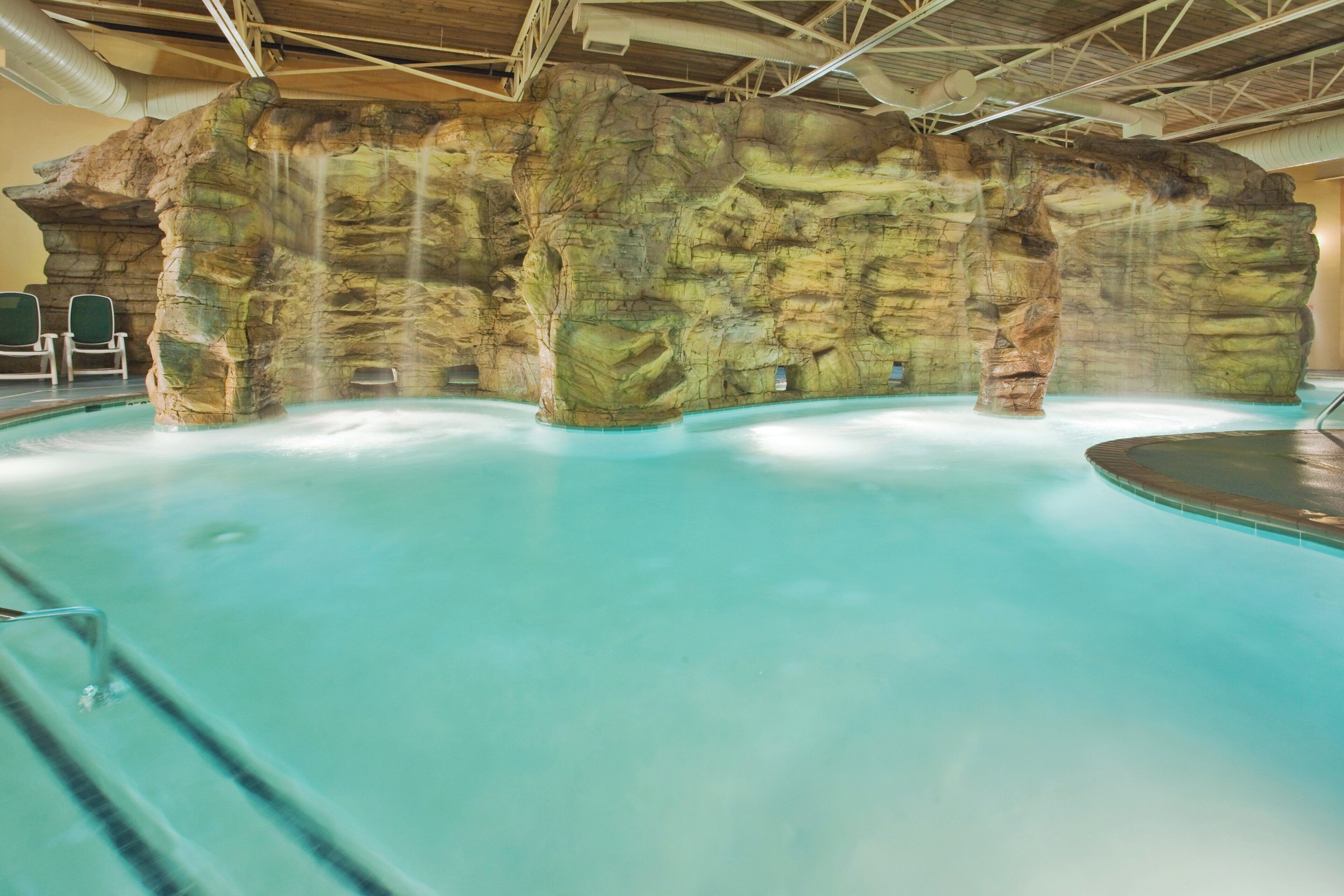 An indoor swimming pool with a rocky wall backdrop and a clear blue pool.