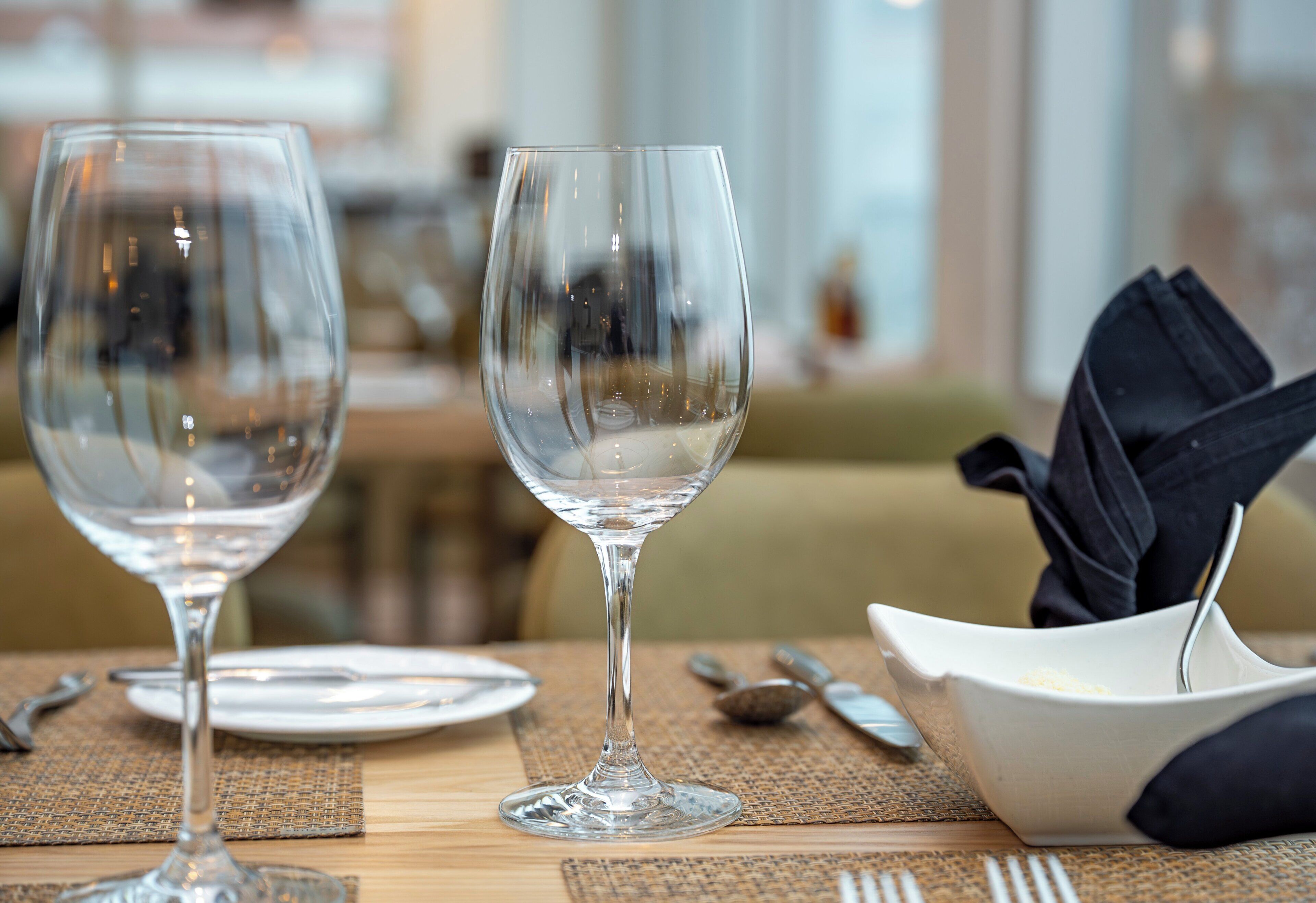 Two empty wine glasses on a table with a napkin, cutlery, and a bowl.