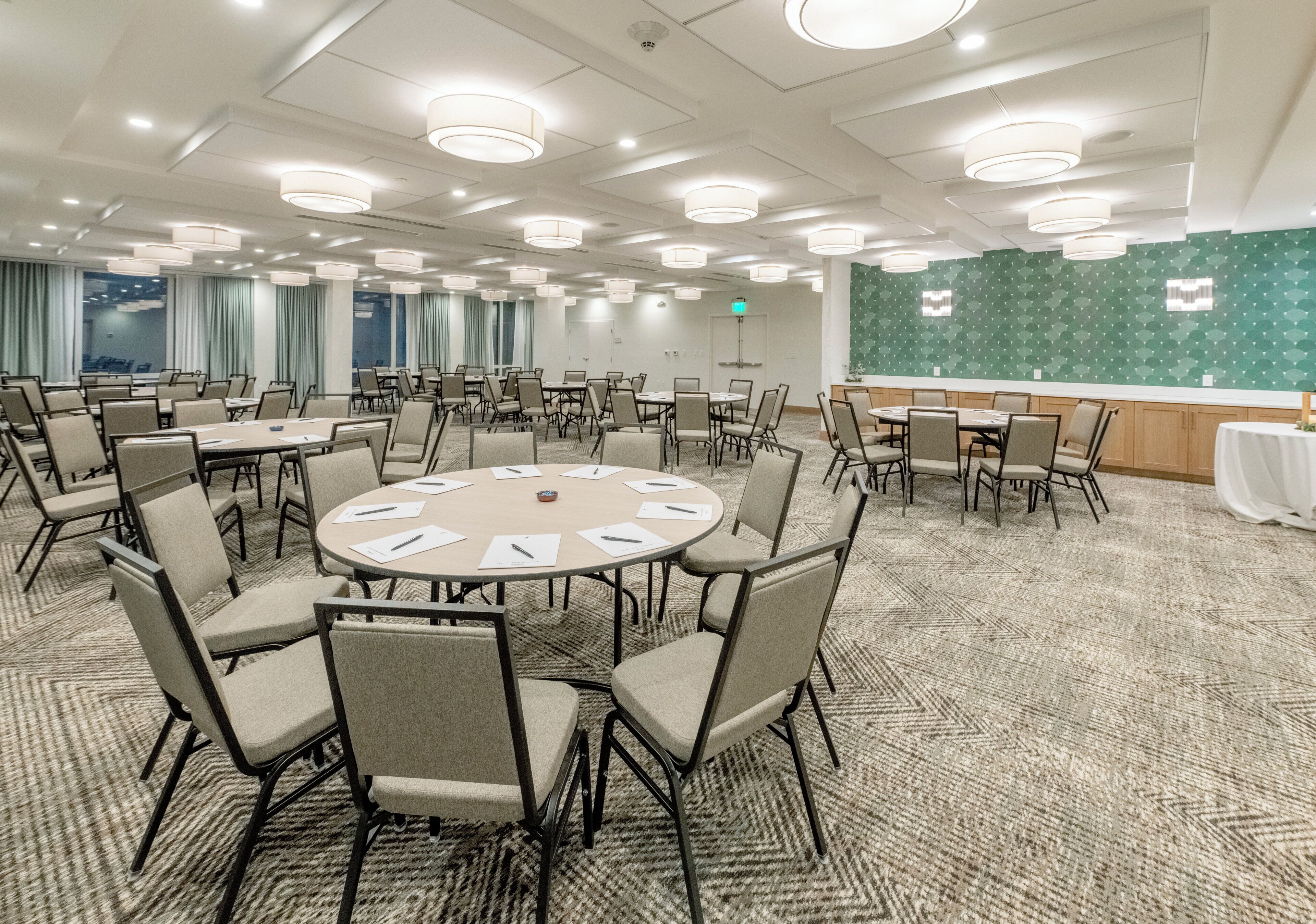 A conference room with round tables, chairs, and a green patterned wall.