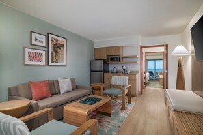 A modern living room with a sofa, coffee table, and chairs, a kitchen area with a microwave and refrigerator, and a view through an open door. - Holiday Inn & Suites Virginia Beach North Beach by IHG (Virginia Beach)