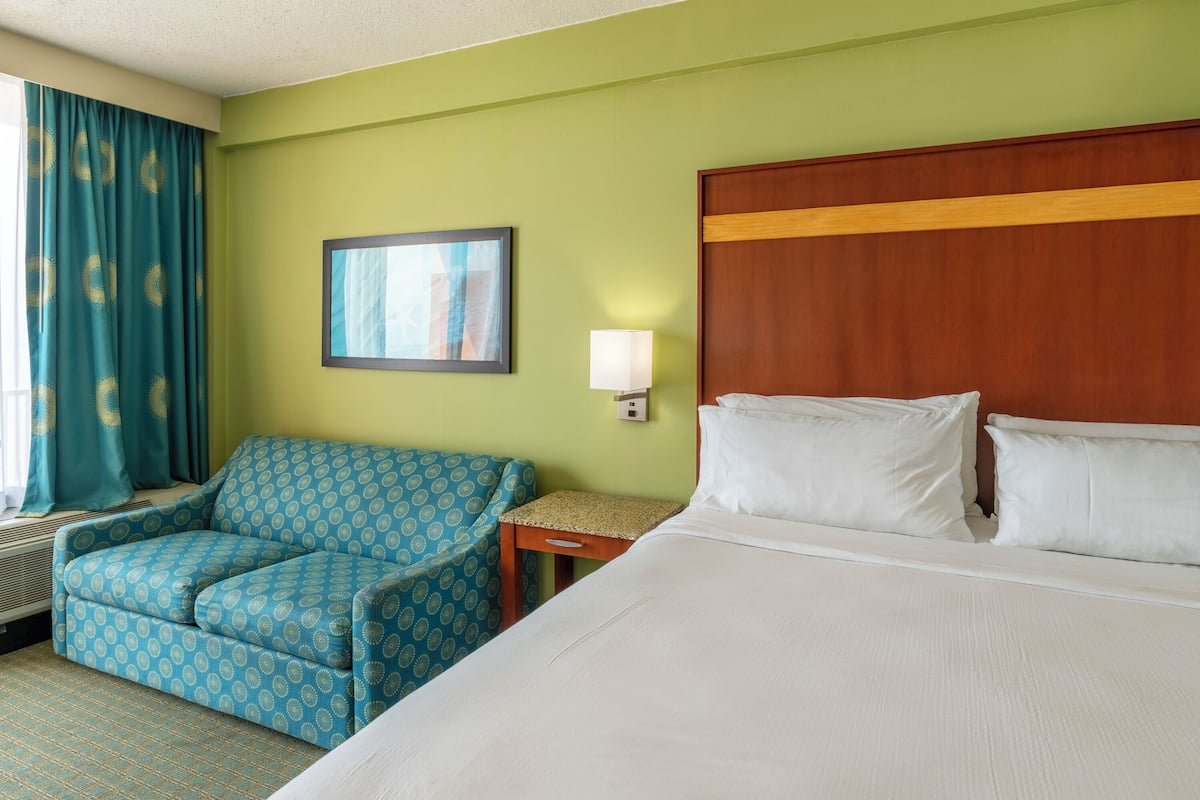A hotel room with a bed, a chair, a nightstand, a lamp, and a window with curtains.