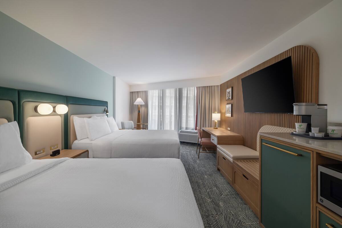 A hotel room with two beds, a desk, a TV, and a minibar.