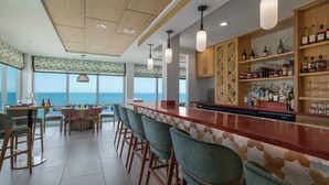 Zona de bar con una barra larga, taburetes y estantes llenos de botellas.