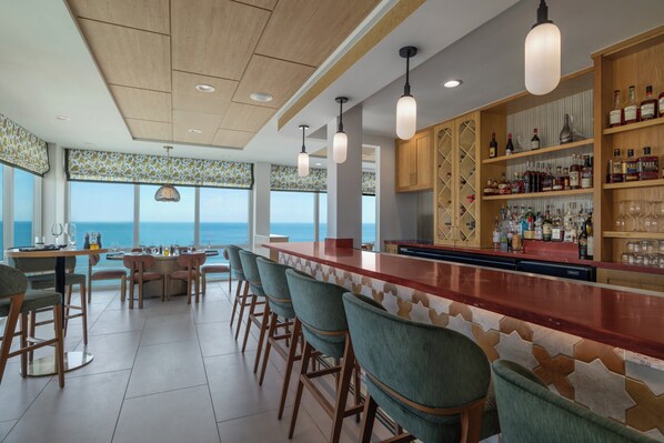 A bar area with a long counter, bar stools, and shelves stocked with bottles. - Holiday Inn & Suites Virginia Beach North Beach by IHG (Virginia Beach)