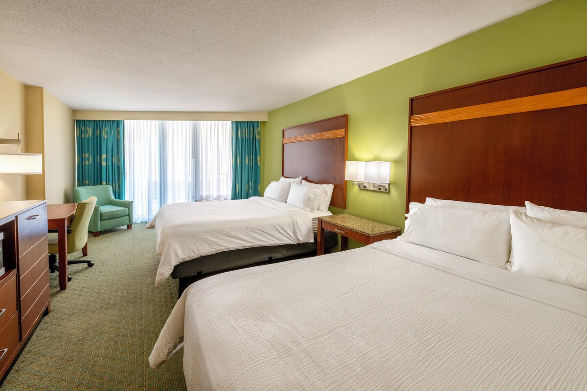 A hotel room with two beds, a desk, a chair, and a window with curtains.
