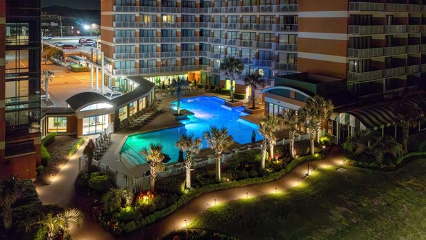 Un hotel con una piscina grande rodeada de palmeras y senderos bien iluminados.