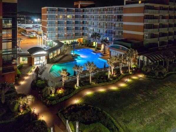 Un hotel con una piscina grande rodeada de palmeras y senderos bien iluminados.