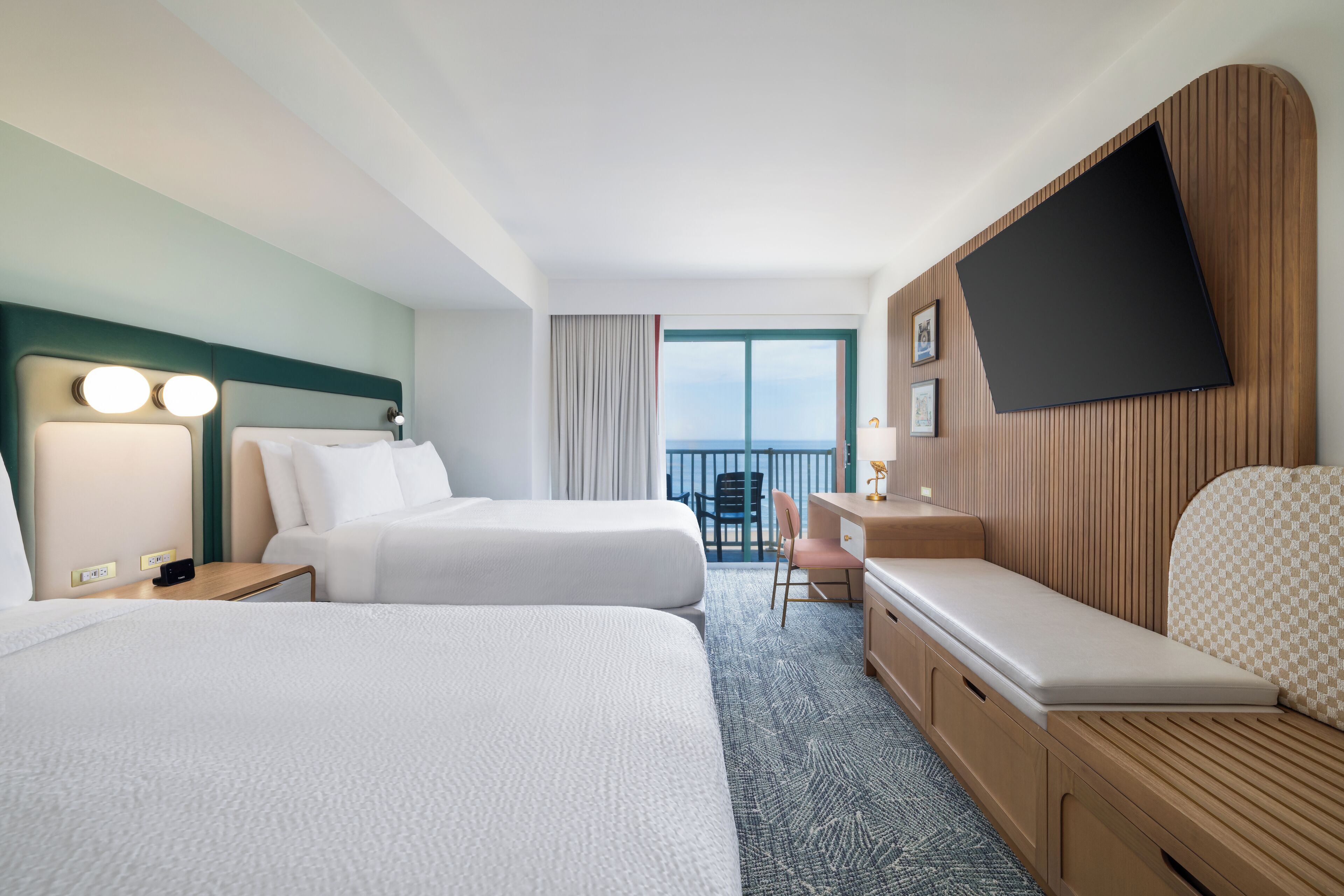 Ein Hotelzimmer mit zwei Betten, einem Schreibtisch, einem Sessel, einem Fernseher und einem Balkon mit Blick.