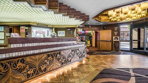Zona de recepción de hotel con mostrador de registro, habitaciones de huéspedes y un vestíbulo con alfombra estampada.