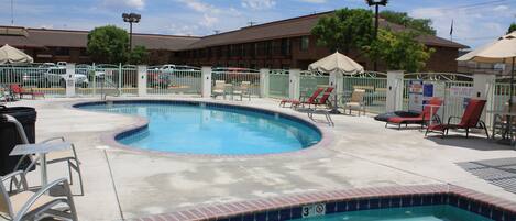 A swimming pool with a tiled edge, surrounded by lounge chairs and umbrellas, with a building in the background.