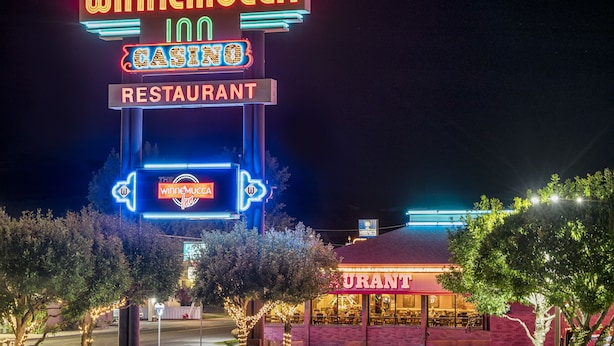 Un letrero iluminado con neón del Casino y Restaurante WinneMucca, con una entrada visible y un área de estar al aire libre.