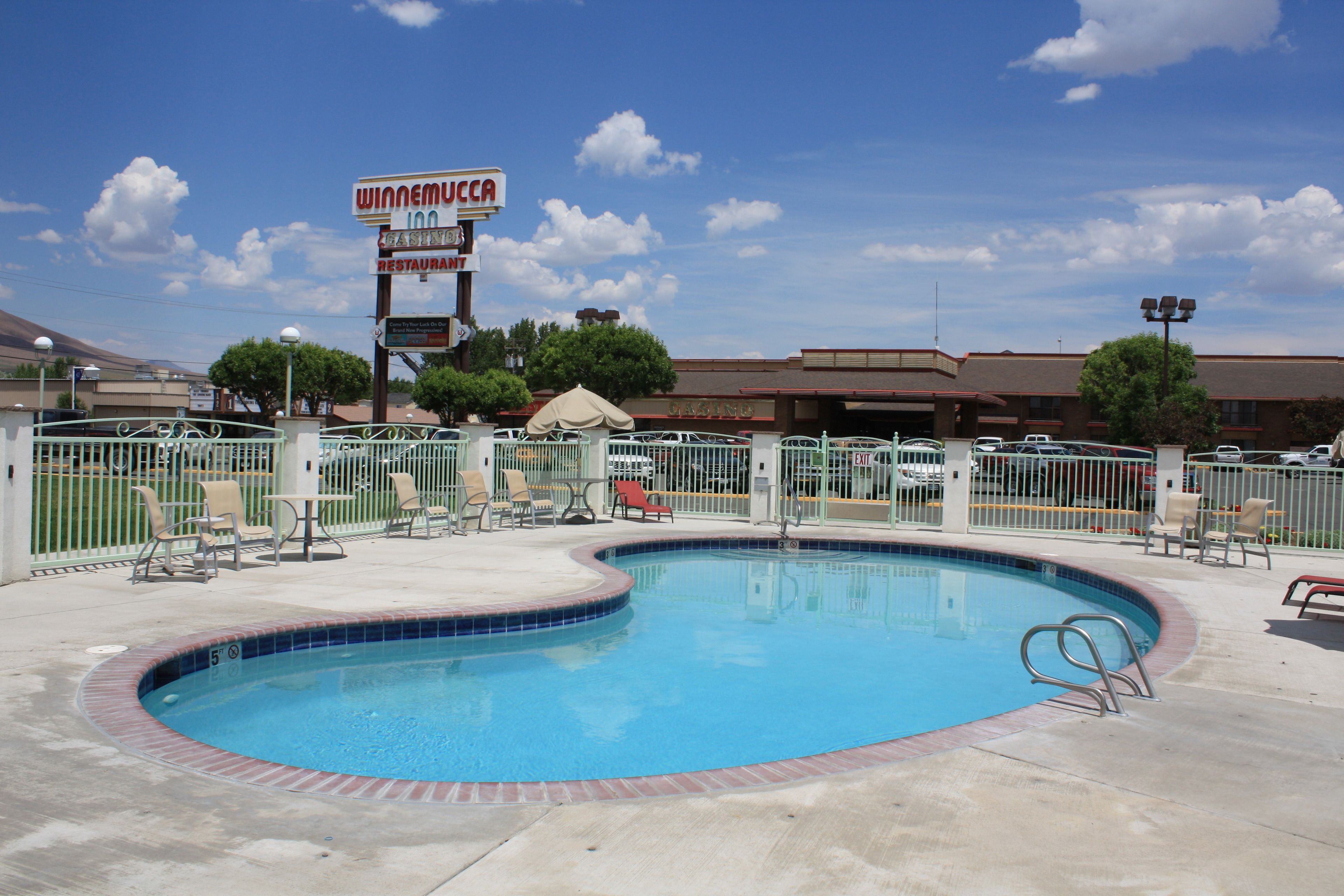 A swimming pool with a fenced area, a restaurant sign, and a building in the background.