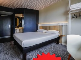 Una habitación de hotel con una cama, una silla, una mesita de noche y un espejo.