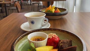Una mesa de comedor con un plato de postre que contiene fruta y un recipiente pequeño de salsa, una taza de café y una pantalla de presentación al fondo.