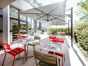 An outdoor seating area with tables and chairs, umbrellas, and a building with large windows in the background.