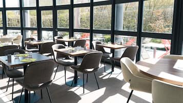 Un espace de restauration moderne, doté de tables et de chaises, de grandes fenêtres et offrant une vue sur l’extérieur.