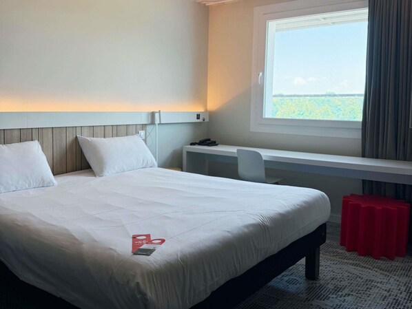 A hotel room with a bed, a desk, a chair, and a window with a view of the outdoors.