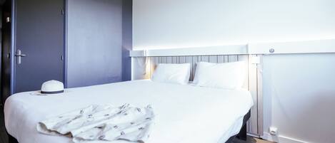 A modern hotel room with a large bed, a bedside table, a wardrobe, and a patterned ceiling.