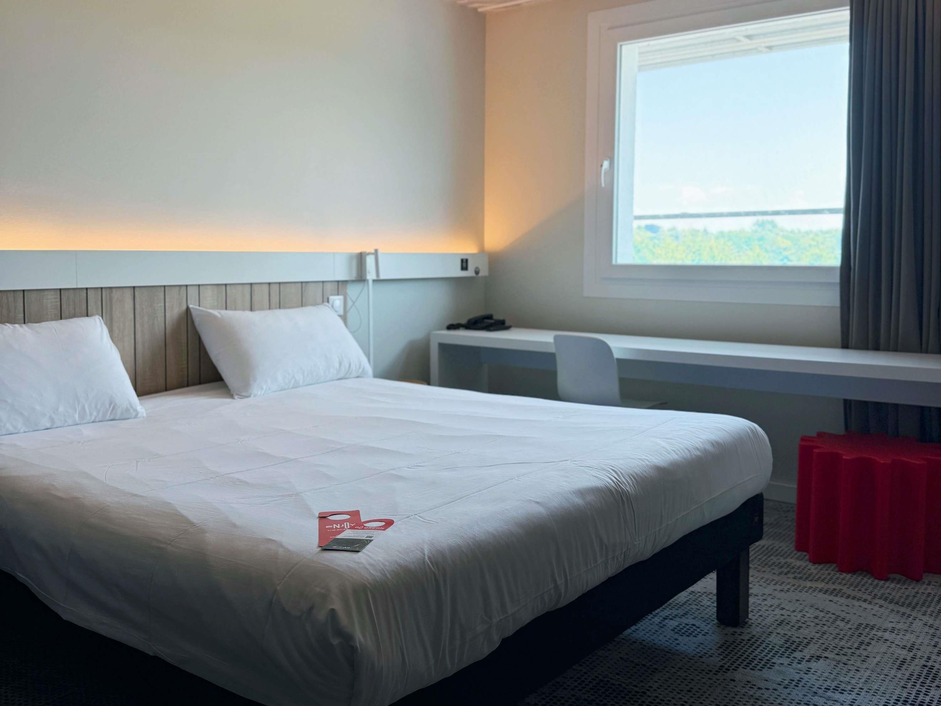 Ett hotellrum med en säng, ett skrivbord och ett fönster med gardiner.