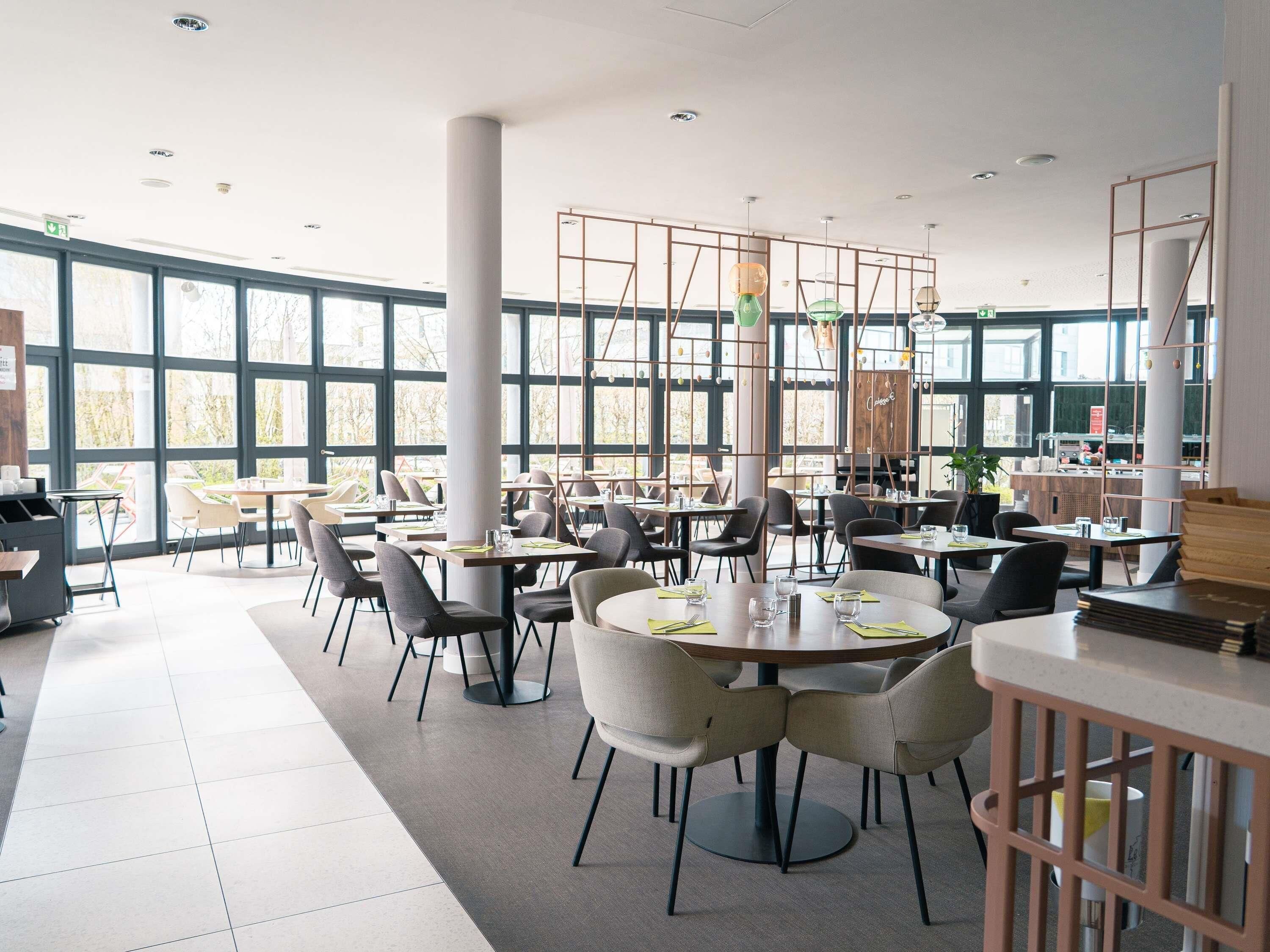 A modern restaurant with large windows, round tables, and a mix of chairs and booths.